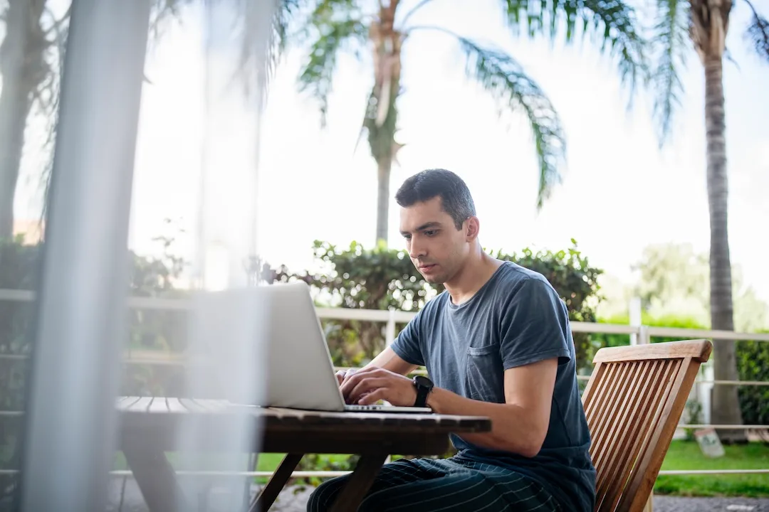 Man explores HELOC options from a laptop in his yard, complete with palm trees.