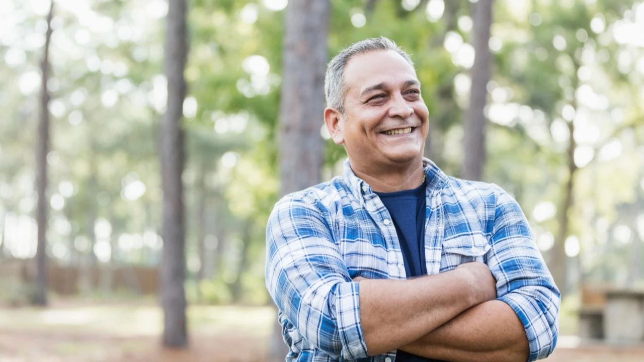 Man standing in forest with arms crossed and smiling