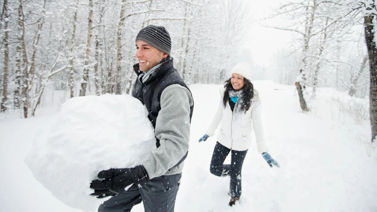 Young man holding snowball with wife.