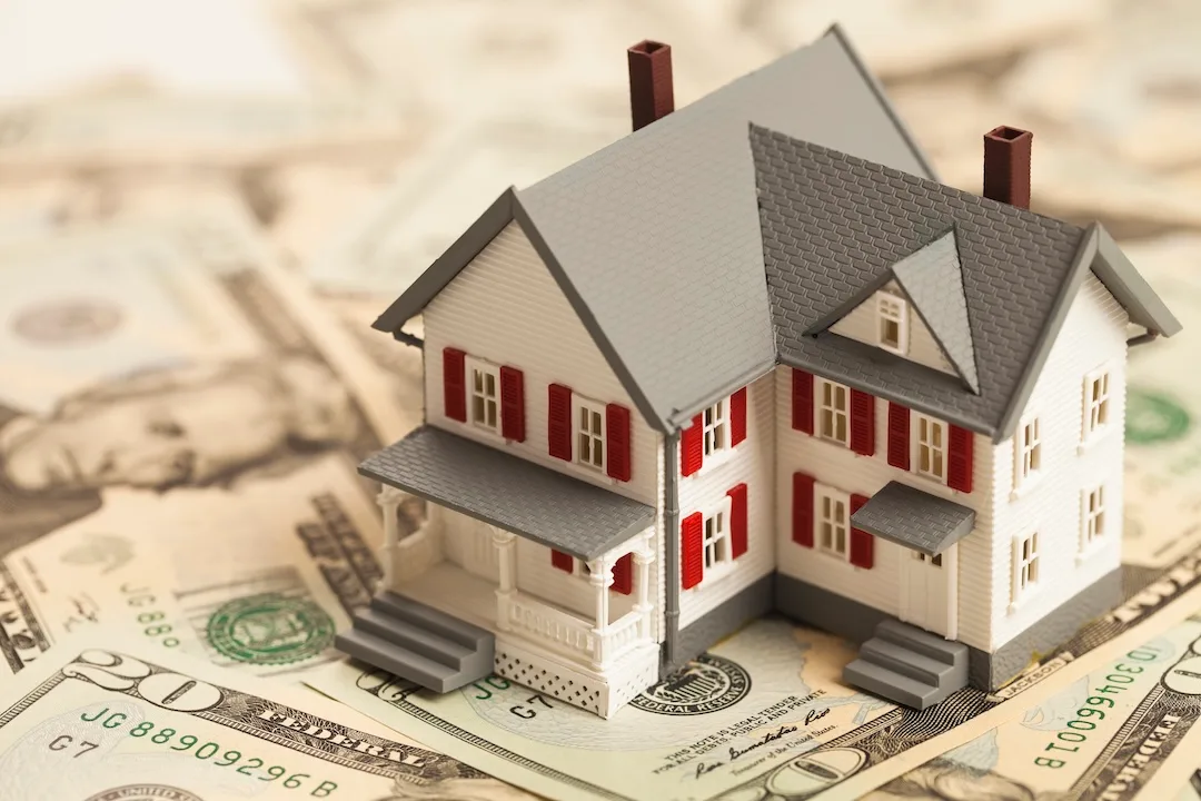 Plastic house on top of pile of money