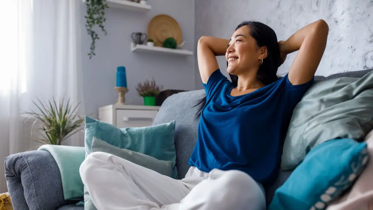 Young woman lounging on sofa with hands behind head and daydreaming