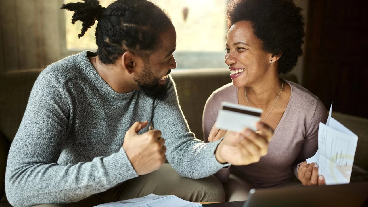 Happy African American couple using credit card while paying their bills online over laptop at home.
