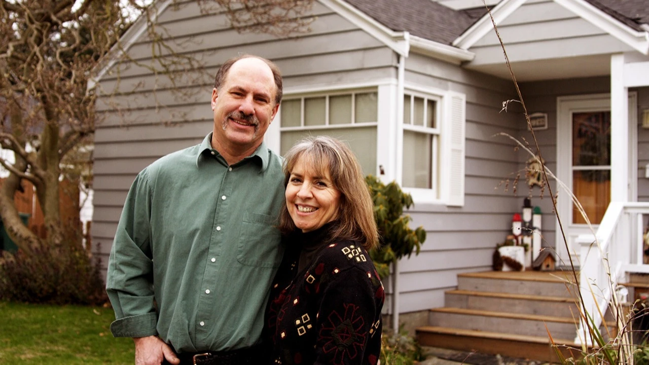A middle age man and a woman embracing standing in front of a house
