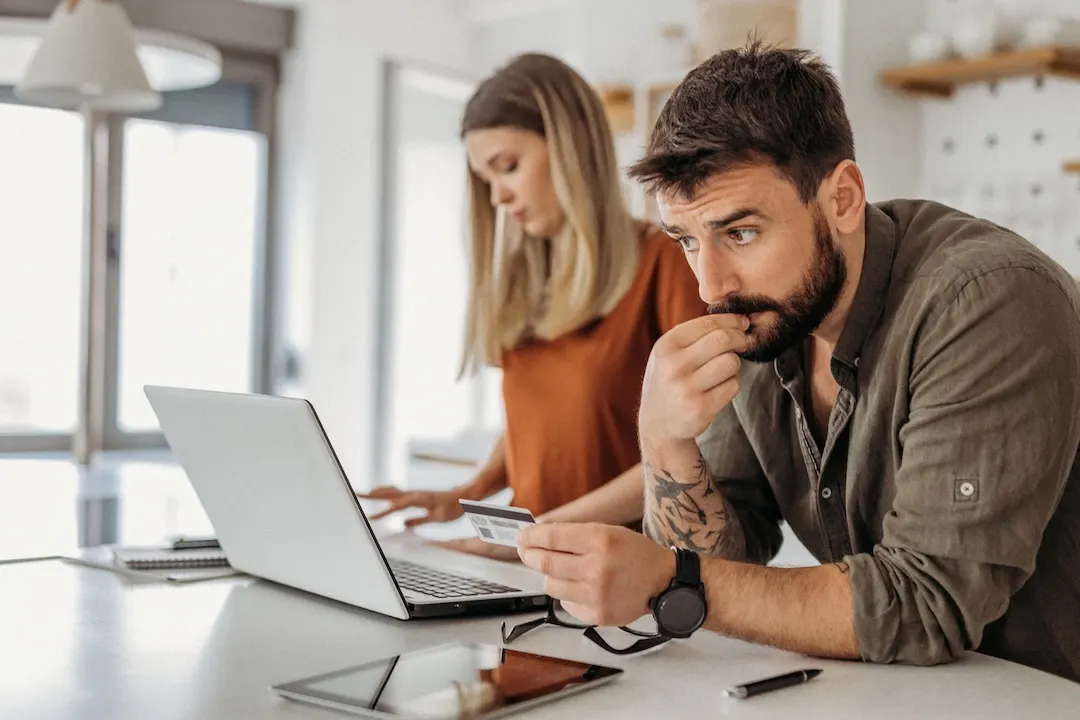 Man holds credit card at laptop with skeptical look
