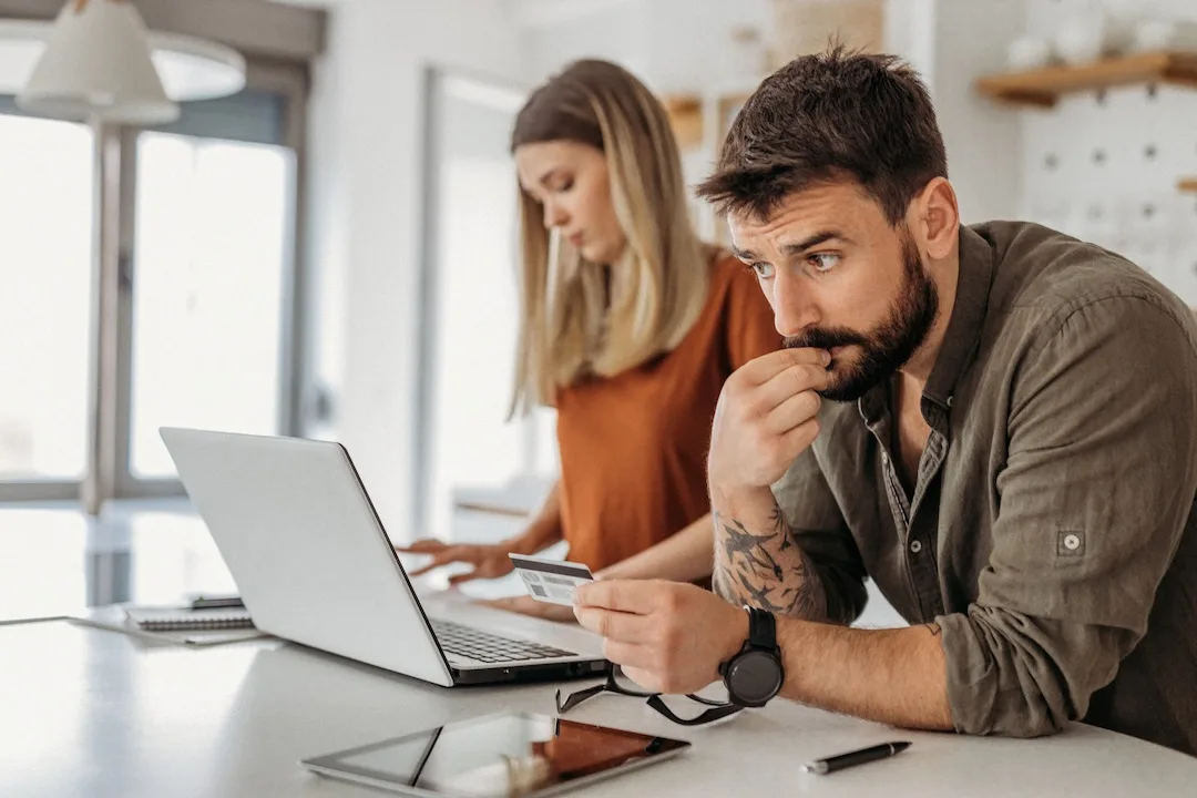 Man holds credit card at laptop with skeptical look