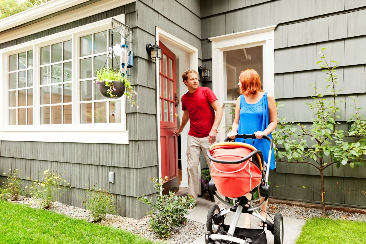Young couple in front of house with baby carriage