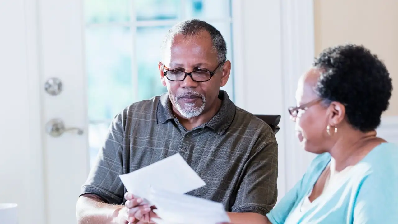 A senior couple in their 60s sitting at a table at home looking through their mail, paying bills, making a financial plan.