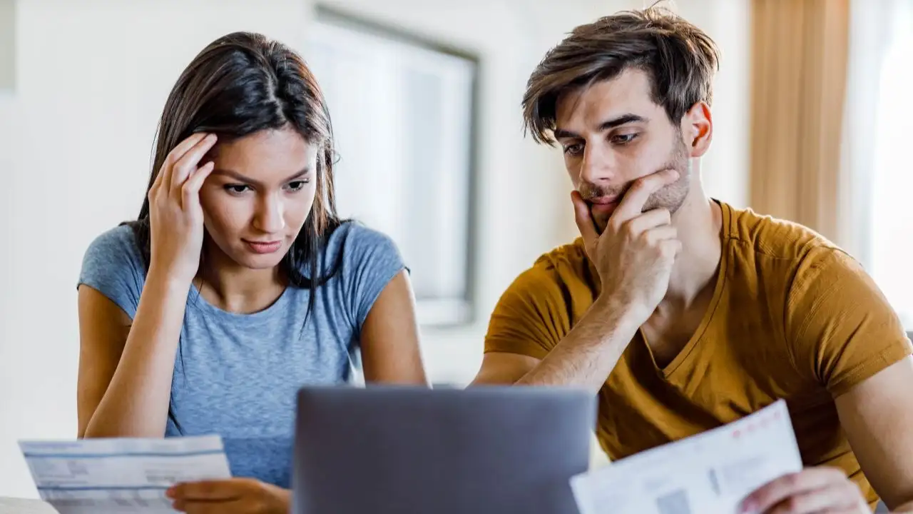 Young worried couple reading their financial bills over laptop at home.