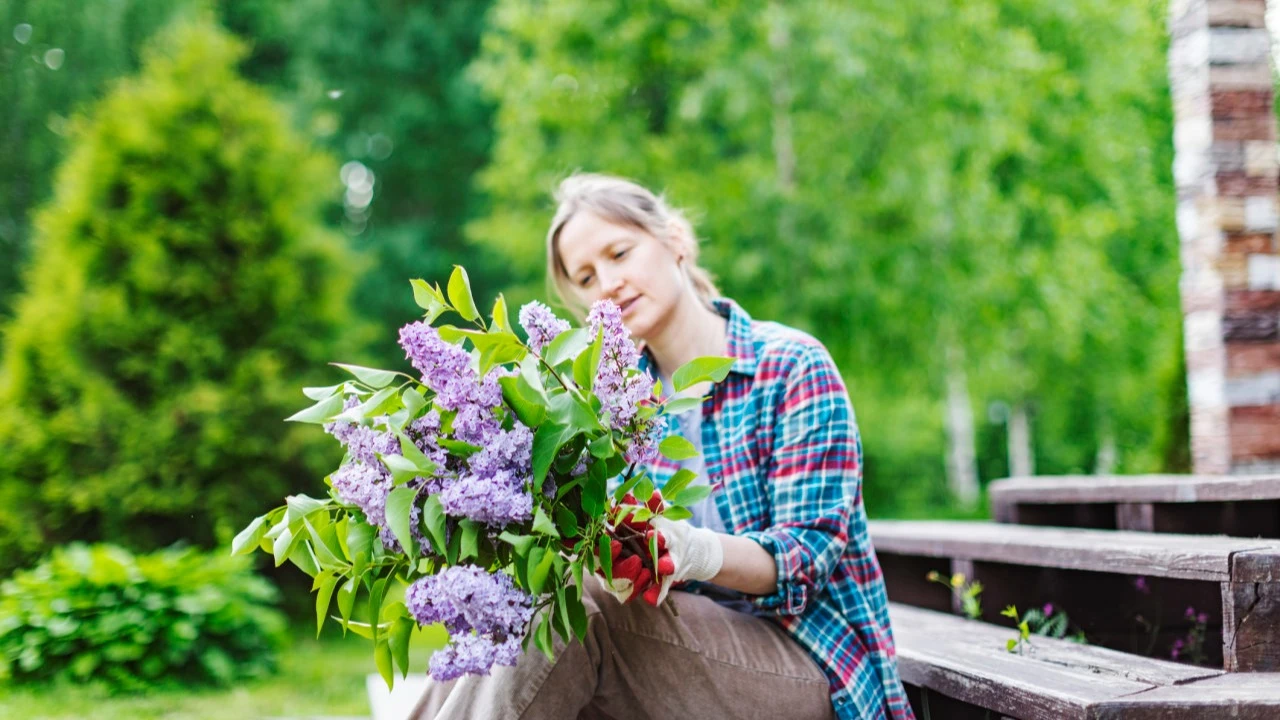 Young adult woman sitting with fresh flowers from her garden on the steps of her house 