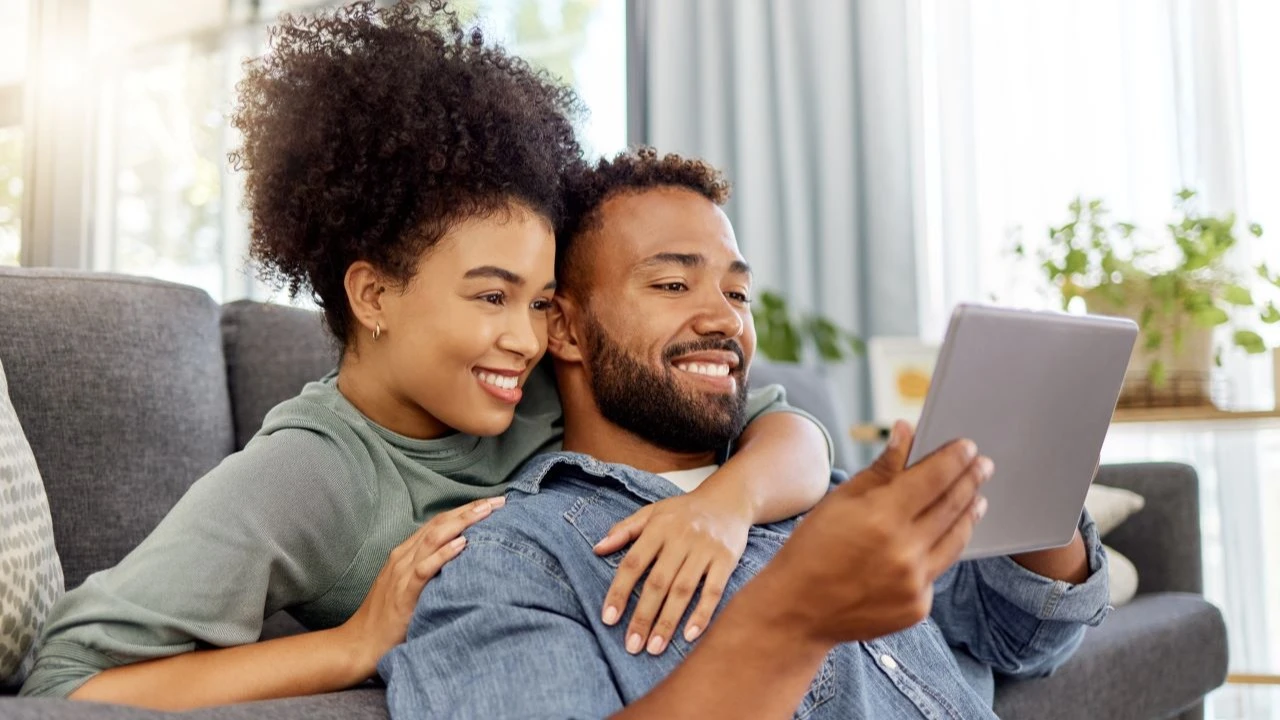  couple smiling while using a digital tablet together at home.