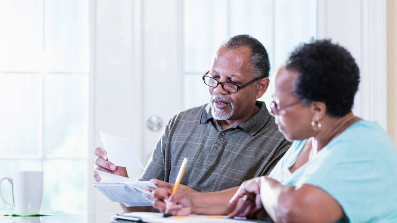 A senior African-American couple in their 60s sitting at a table at home looking through their mail, paying bills, making a financial plan.