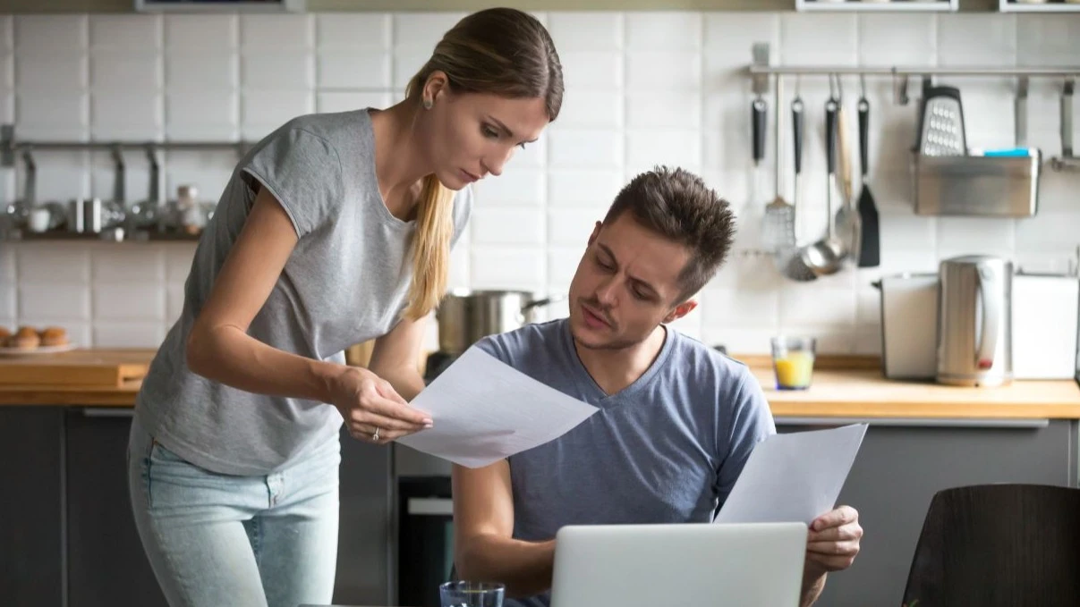 Serious millennial couple worried about high utility bills or rent payment reading papers in kitchen