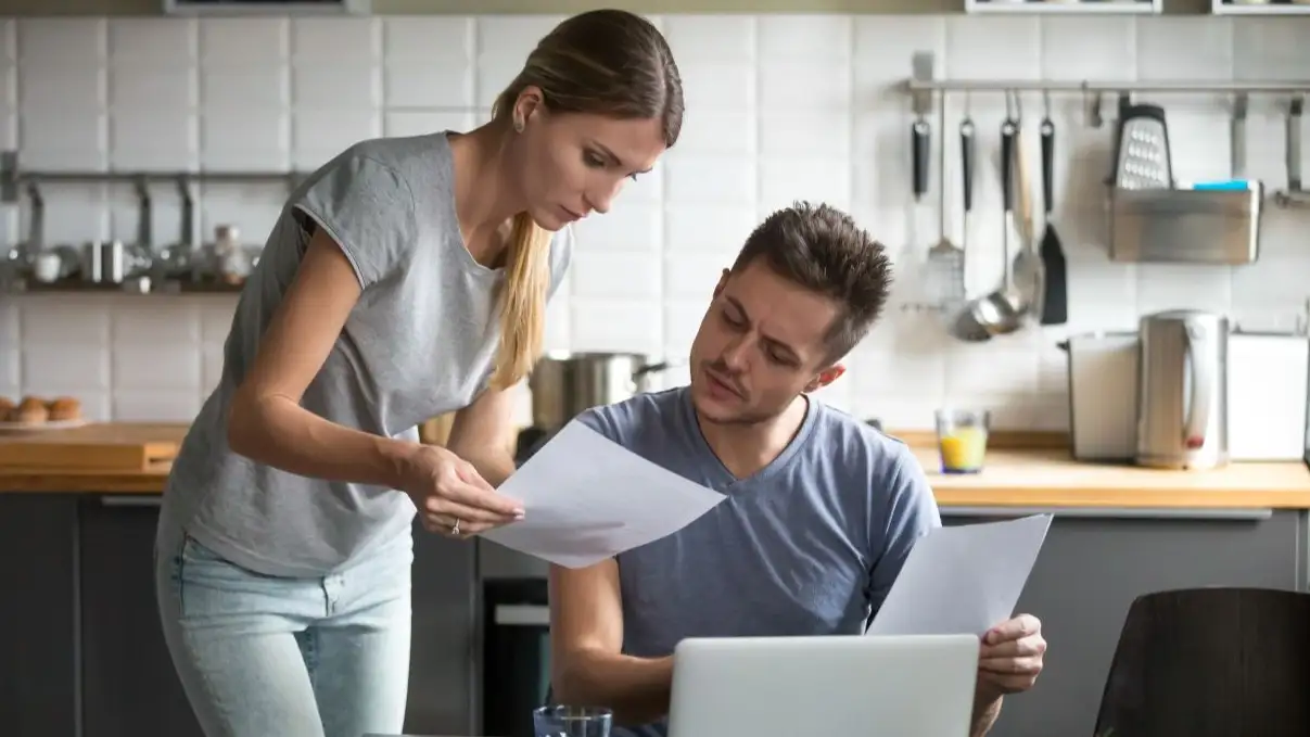 Serious millennial couple worried about high utility bills or rent payment reading papers in kitchen