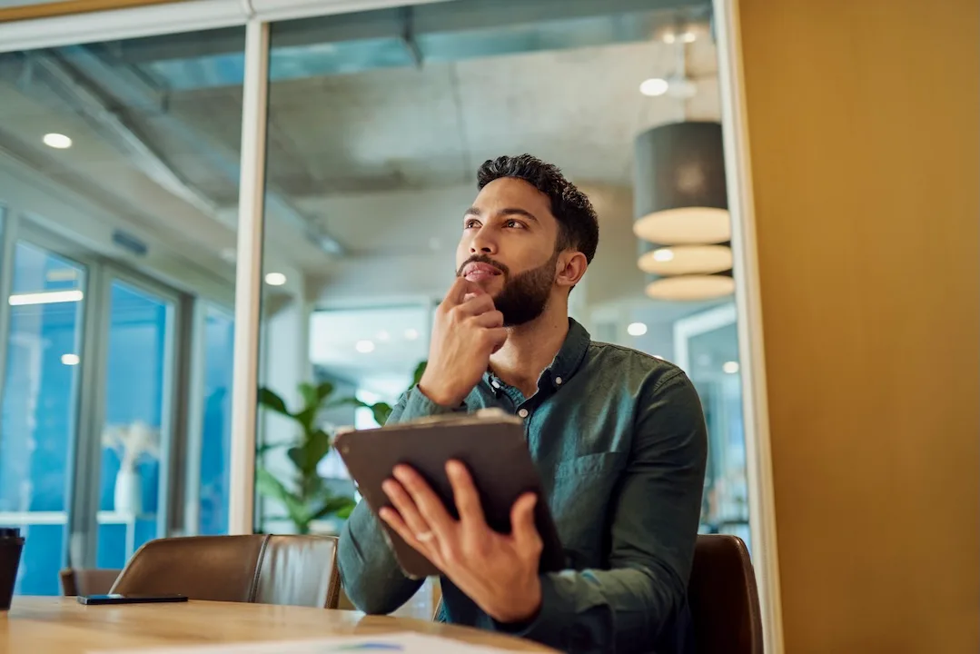 Young man contemplates his options while holding a tablet.