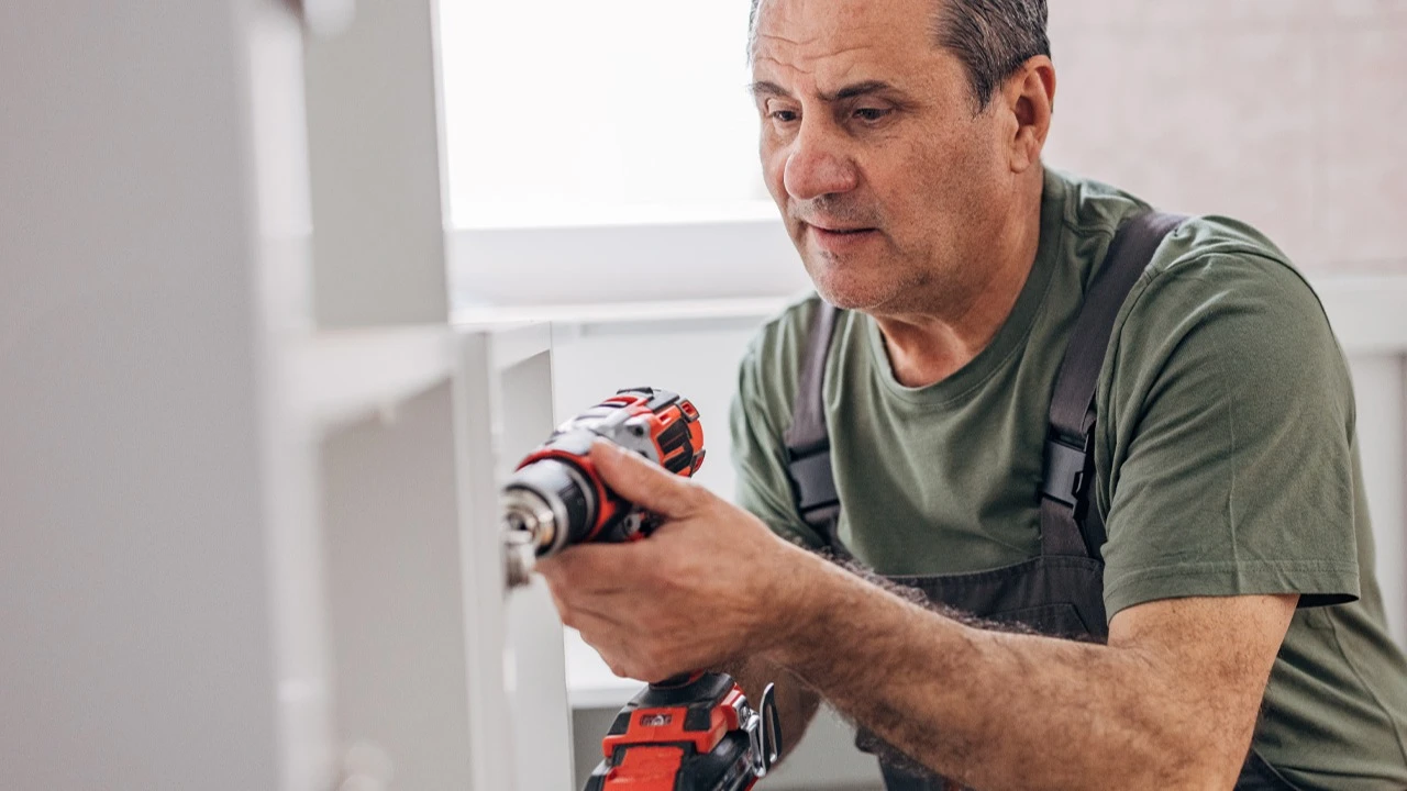 Man with a green shirt holding a power drill and fixing cupboards