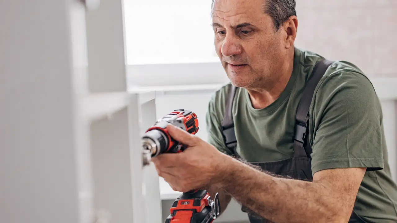 Man with a green shirt holding a power drill and fixing cupboards