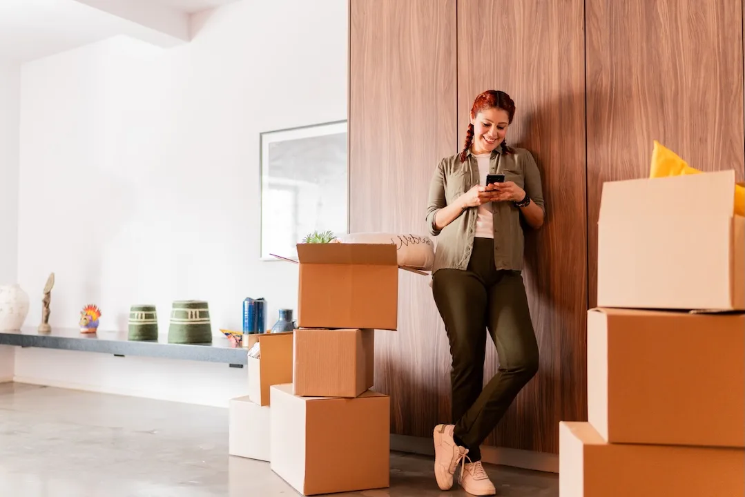 Woman uses smartphone surrounded by moving boxes